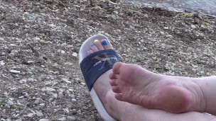 Legs with a pedicure sunbathe on the beach. Foot fetish in slippers